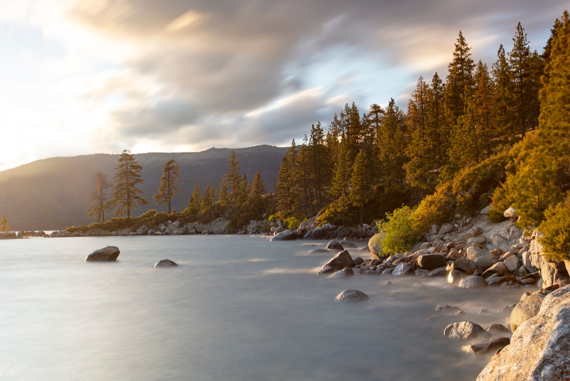 Paysage paisible du lac Tahoe avec des pins et un rivage rocheux au coucher du soleil.