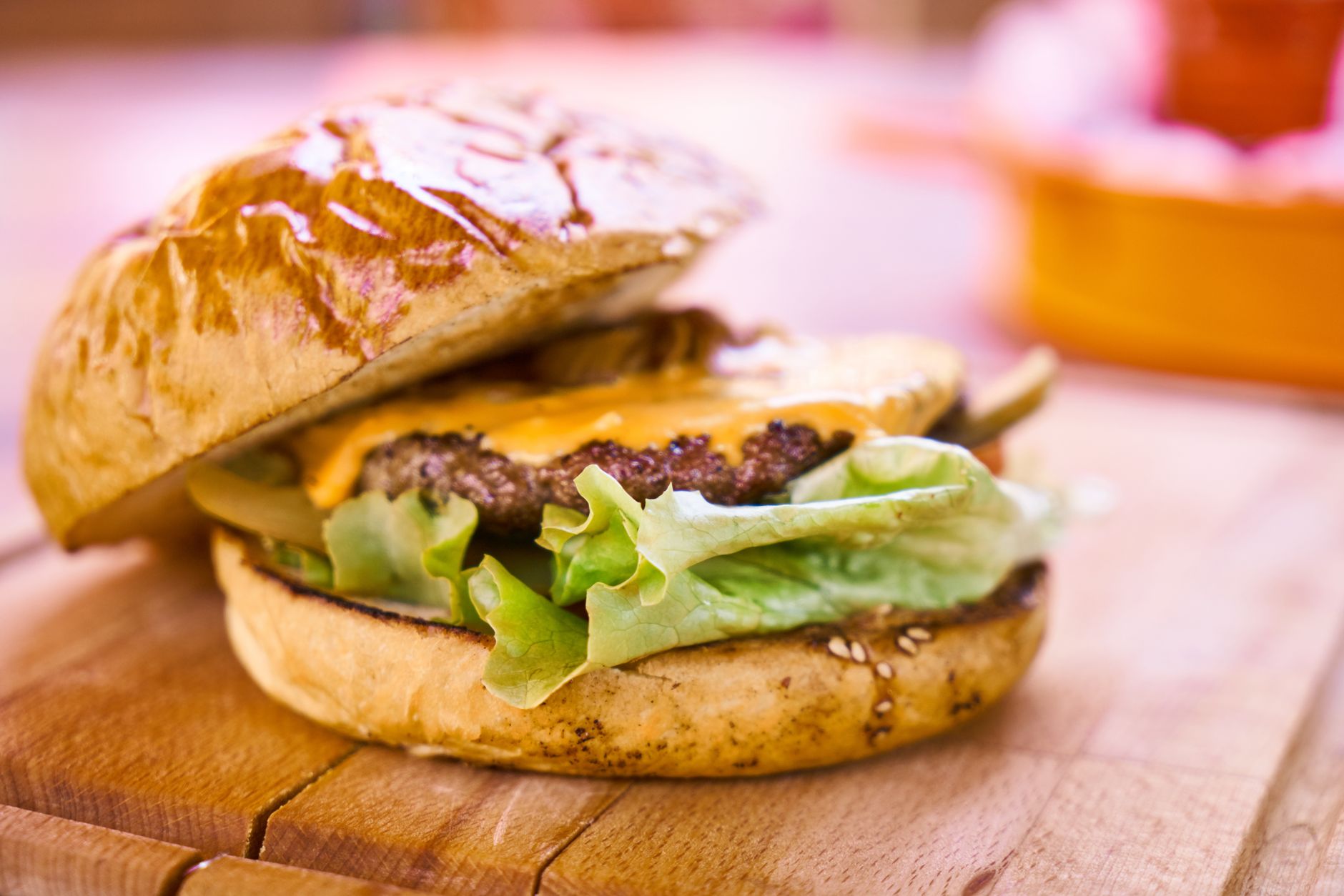 Gros plan d’un hamburger avec steak, fromage fondu et laitue, posé sur une planche en bois.
