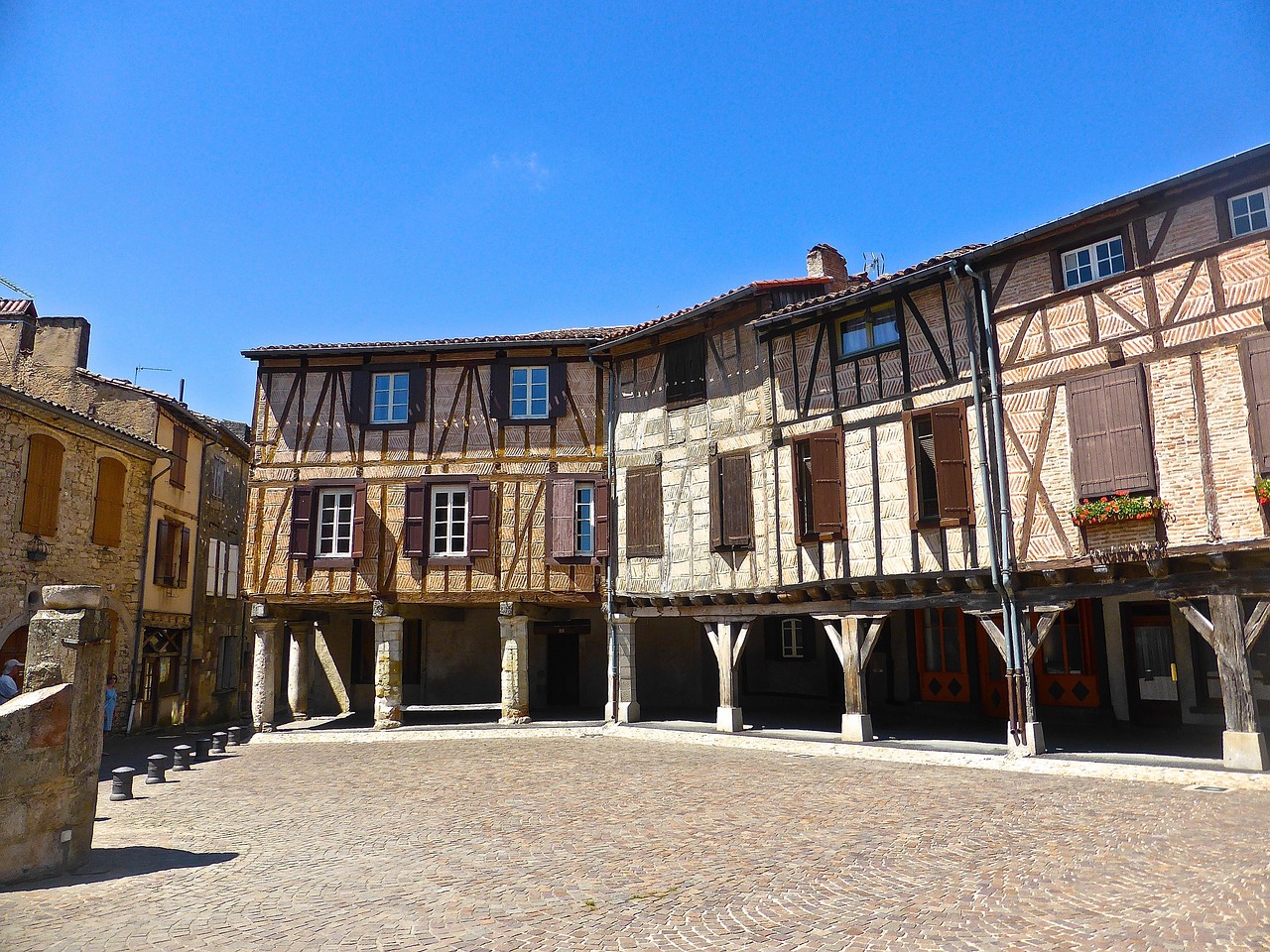 Maisons à colombages posées sur des piliers de bois autour d'une place pavée
